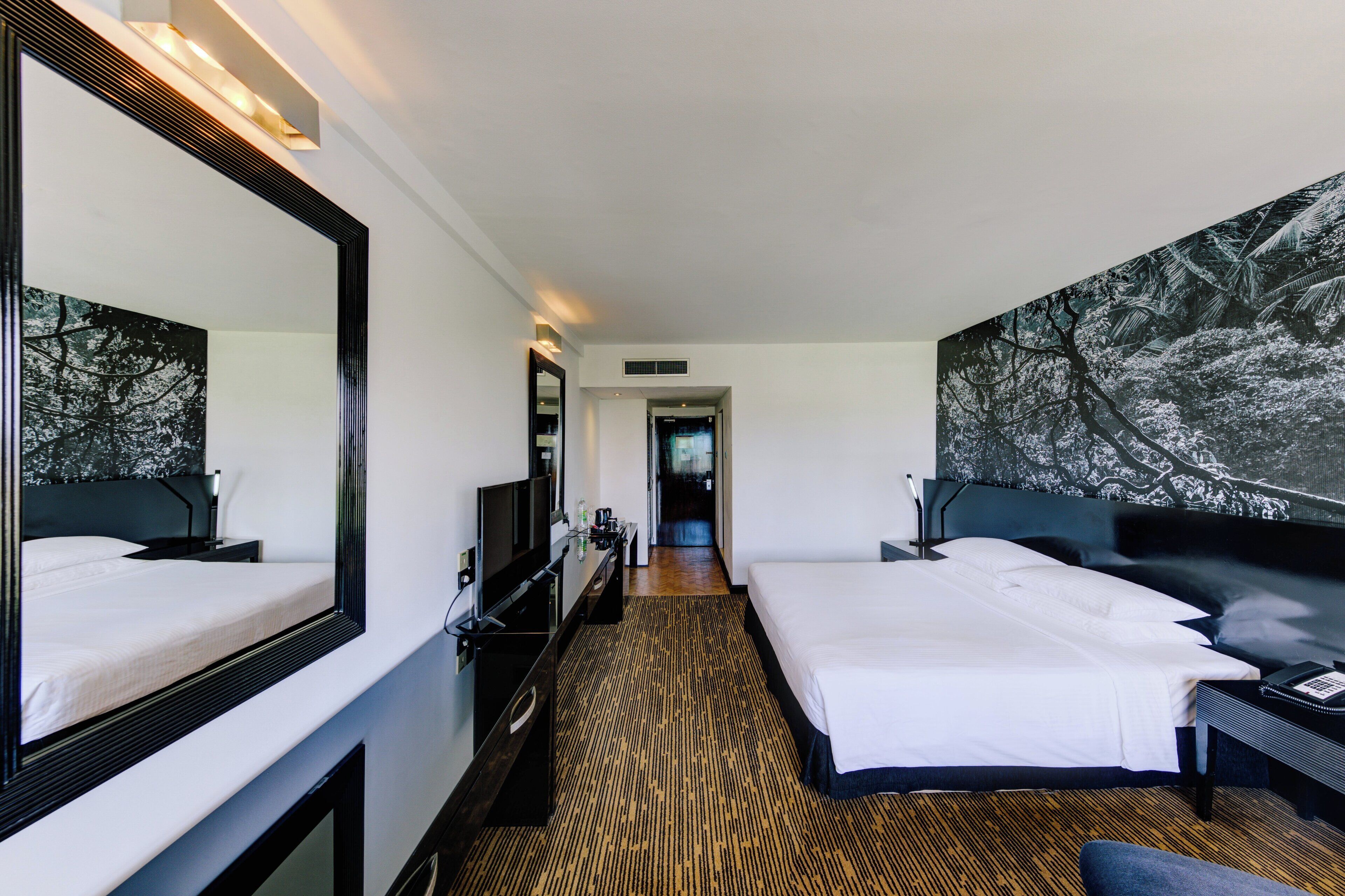 Habitación de hotel con dos camas, un espejo grande, una televisión y un cuadro en la pared.