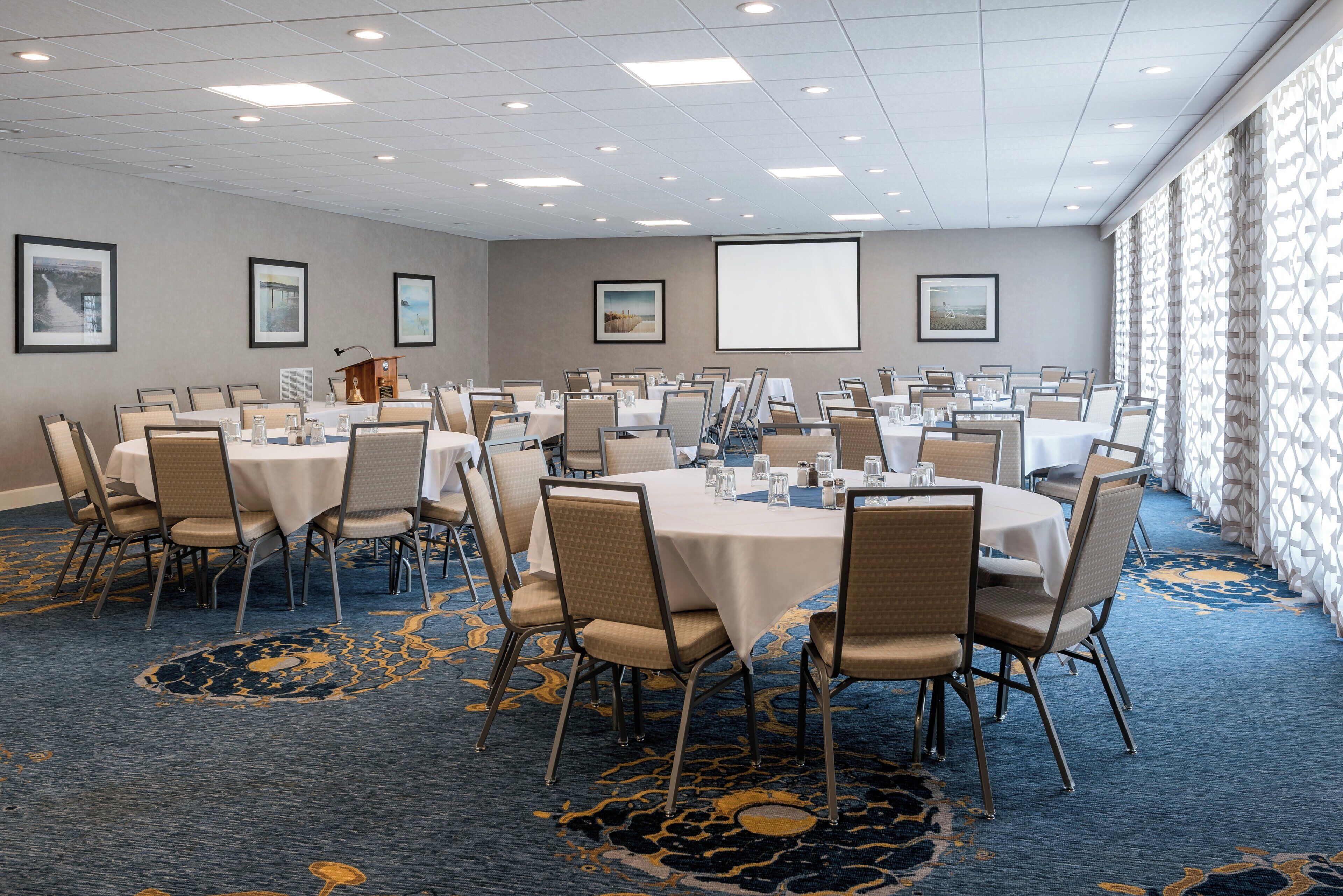 A conference room with multiple tables and chairs, a podium, and a projector screen.