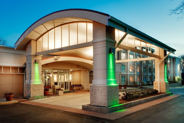 A hotel entrance with a curved roof, large windows, and green lighting on the columns.