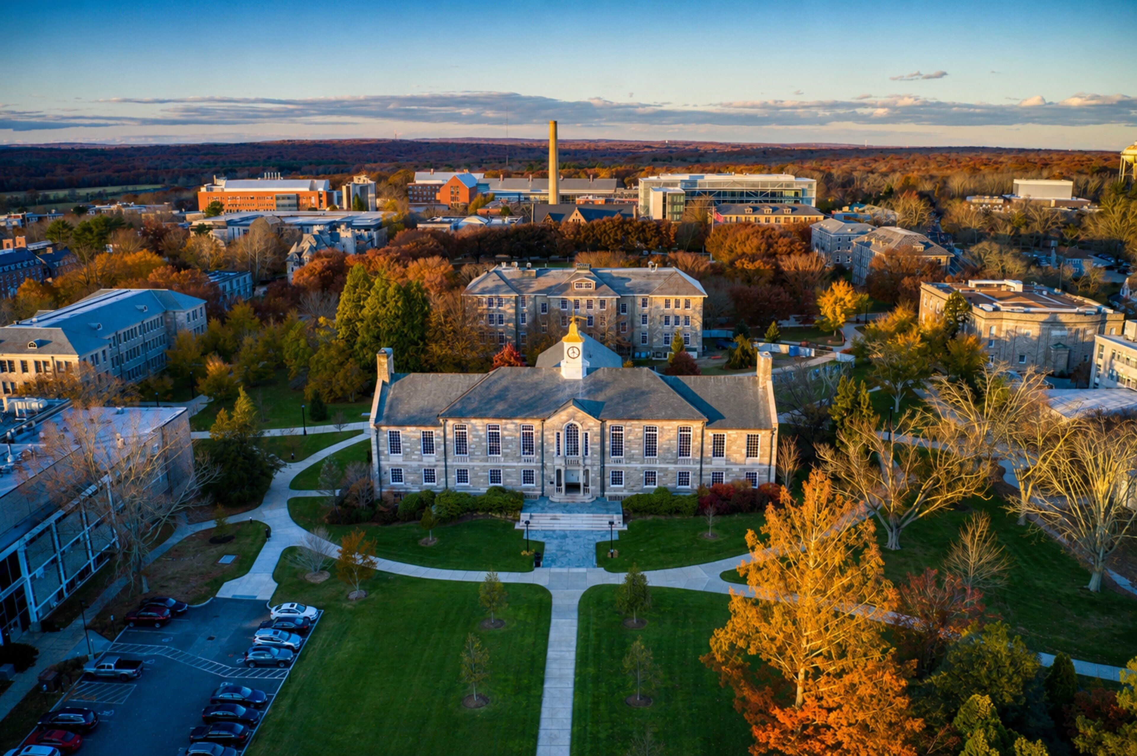 A large institutional building with a central clock tower, surrounded by a well-maintained lawn and parking area.