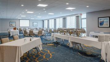 A conference room with multiple tables, chairs, a projector screen, and a buffet setup.