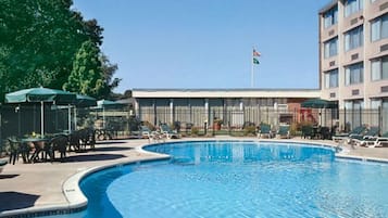 A swimming pool with lounge chairs and umbrellas, a building with a flag, and a clear sky.