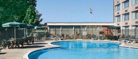 A swimming pool with lounge chairs and umbrellas, a building with a flag, and a clear sky.