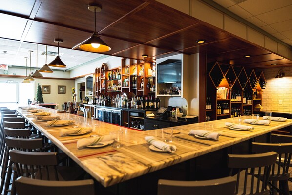 A bar area with a long counter, multiple seating arrangements, and a variety of bottles and glasses on shelves. - Holiday Inn South Kingstown (Newport Area) by IHG (Saunderstown)