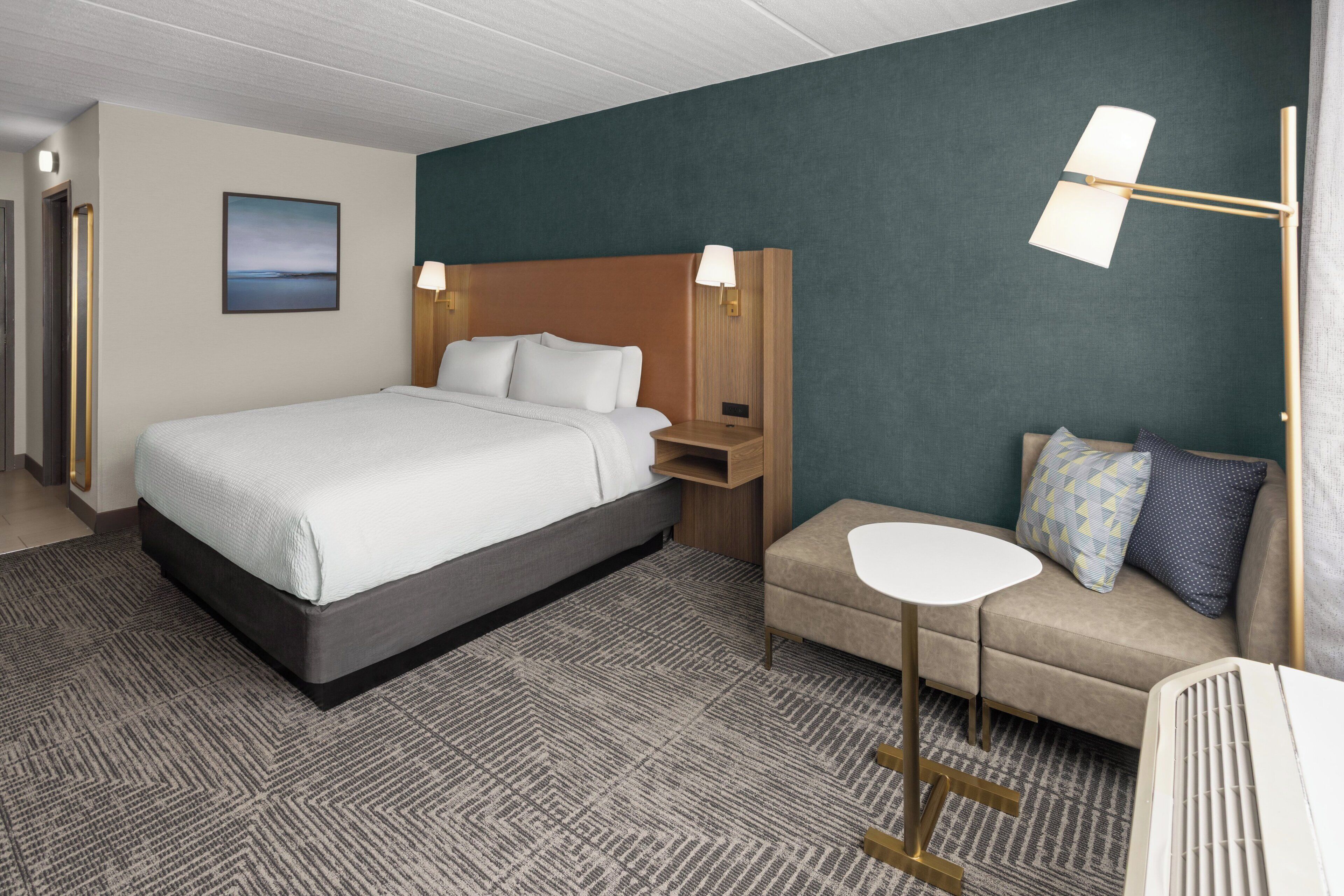 Ein Hotelzimmer mit einem Bett, einem Sofa, einem kleinen Tisch und einer Lampe.