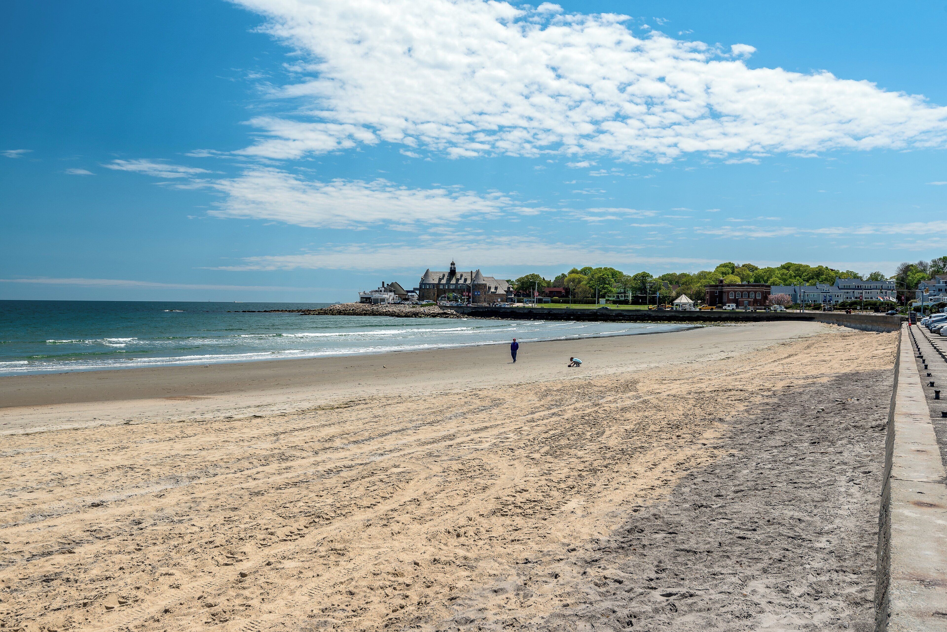 A beach with a clear sky, a sandy shore, and buildings in the background.