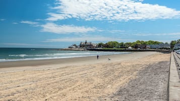 A beach with a clear sky, a sandy shore, and buildings in the background.