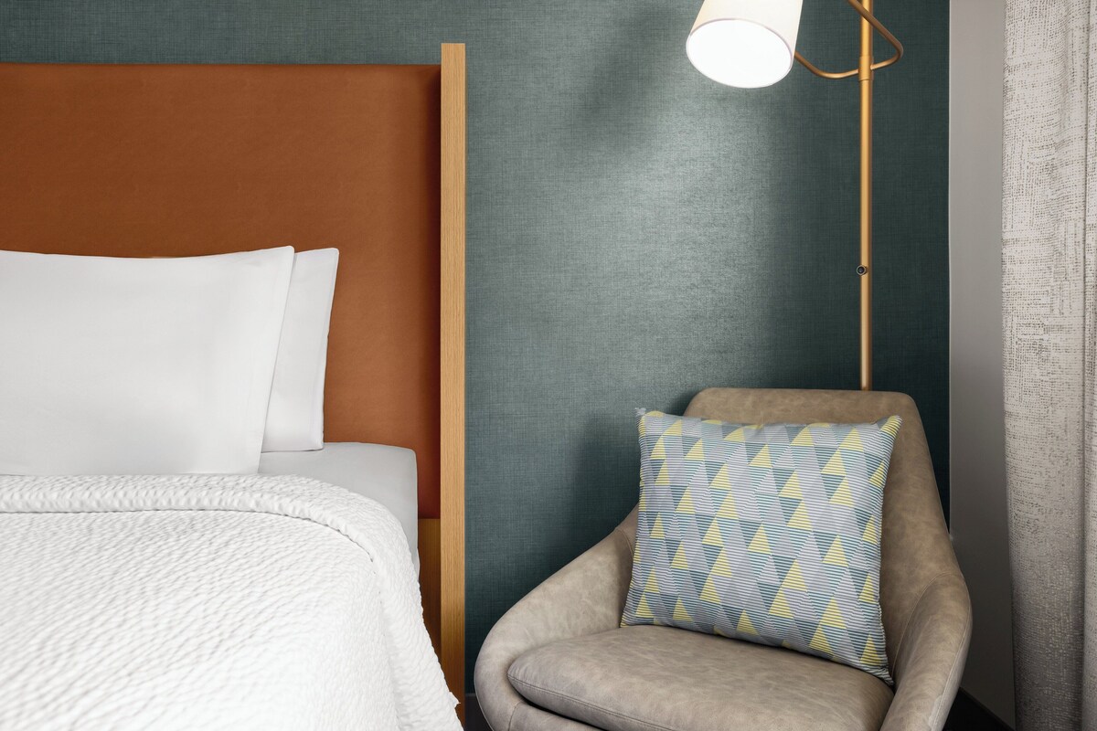 Une chambre d’hôtel avec un lit, une chaise dotée d’un coussin à motifs et une lampe sur pied.