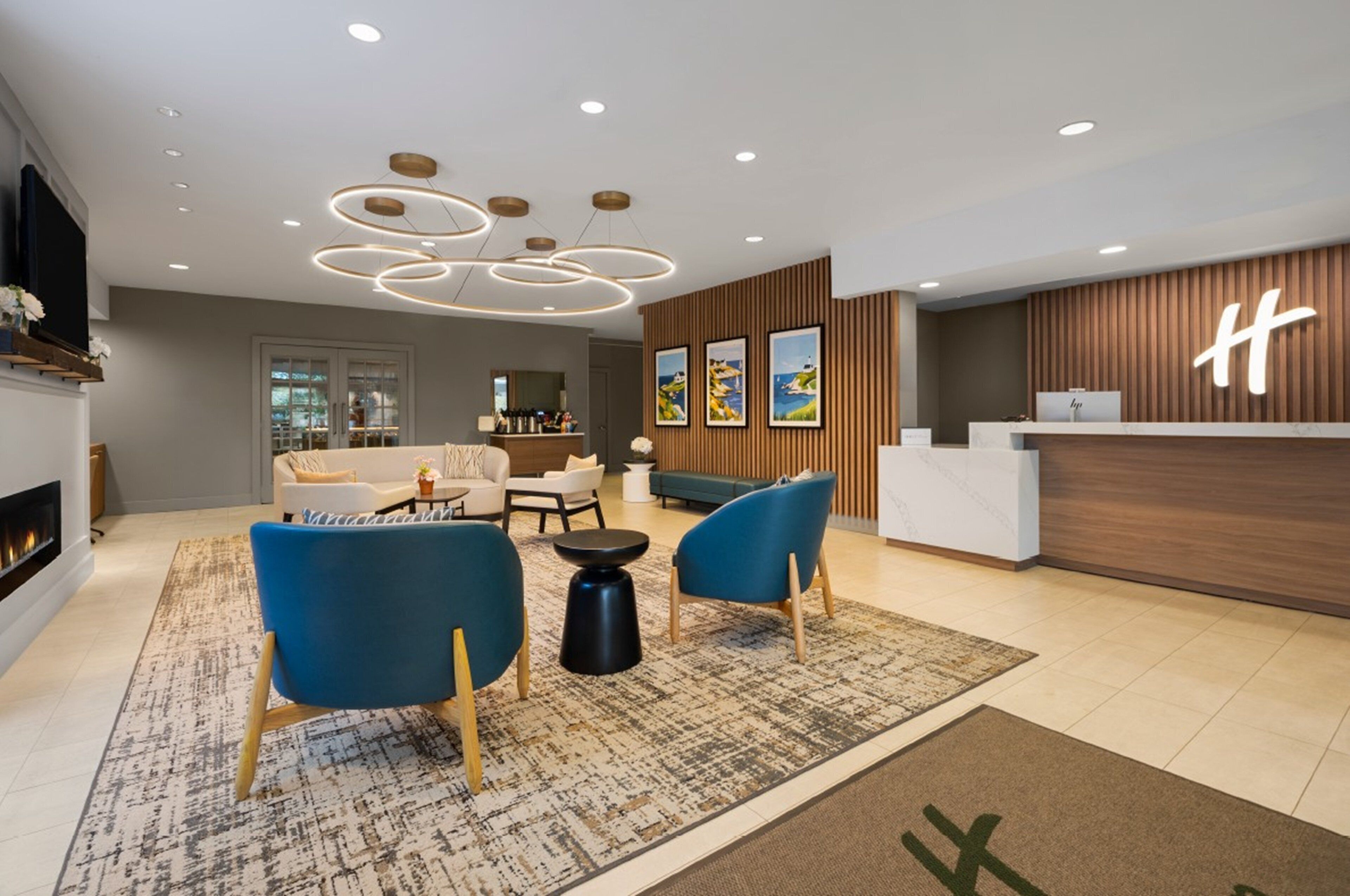A modern hotel lobby with a reception desk, seating area, and a fireplace.