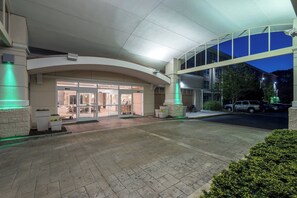 Ein Hotel mit Eingangsbereich, überdachtem Gang, Glastüren und Parkplatz.