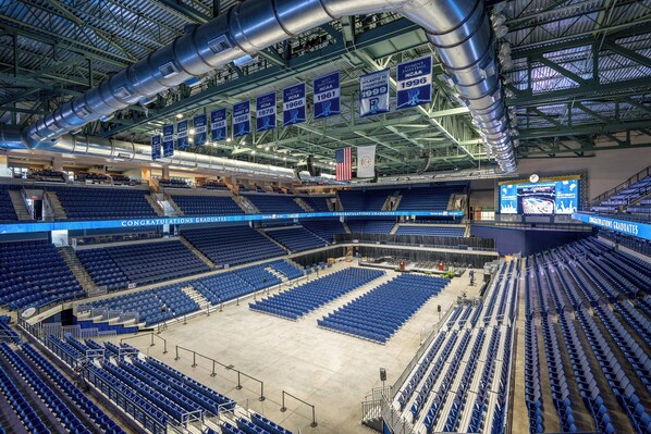 A large indoor stadium with multiple tiers of seating, a central stage, and a high ceiling with visible structural beams and ventilation ducts.