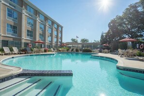 Piscina com espreguiçadeiras e guarda-sóis, rodeada por um edifício com várias janelas.