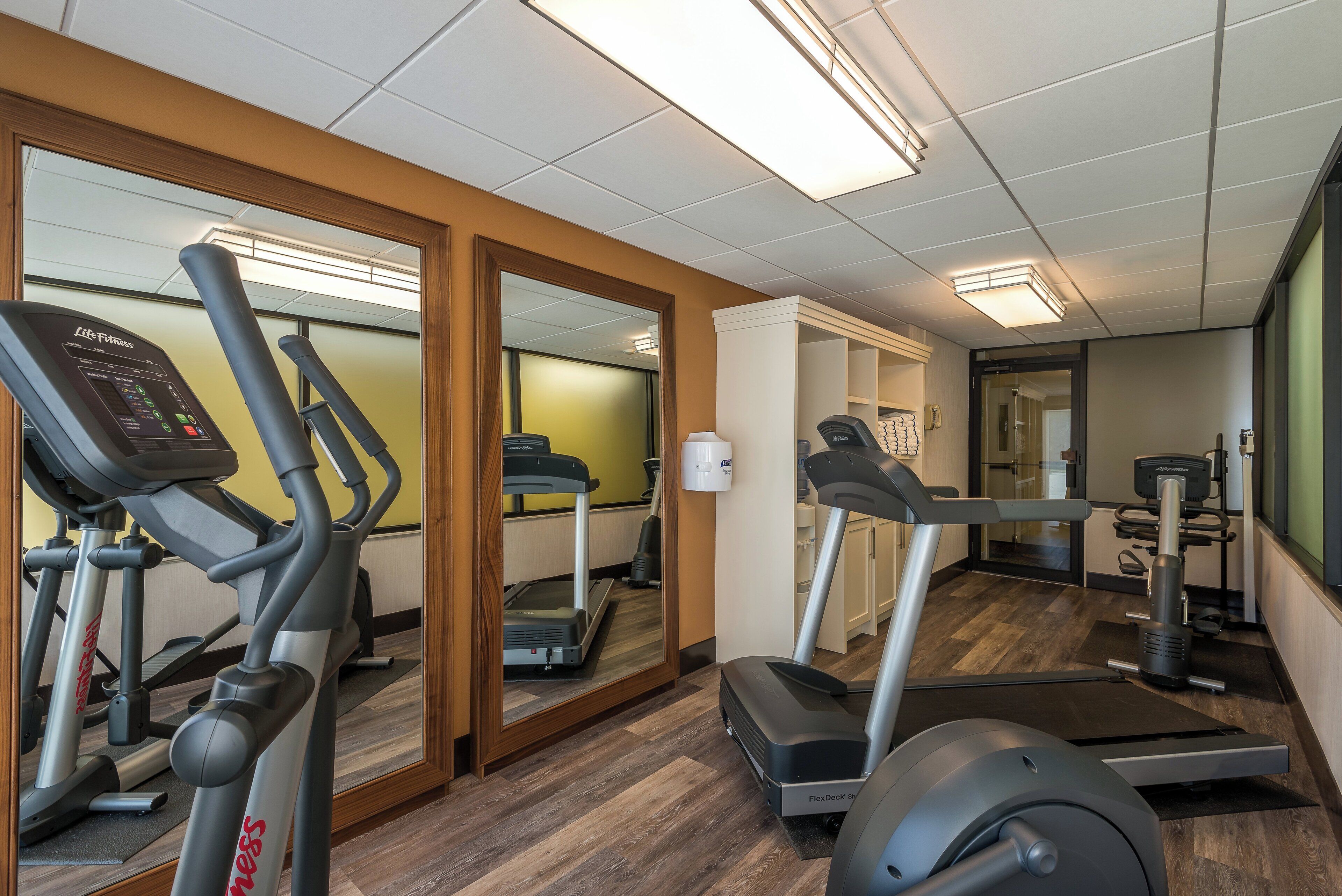 A gym with cardio machines, mirrors, and a wooden floor.