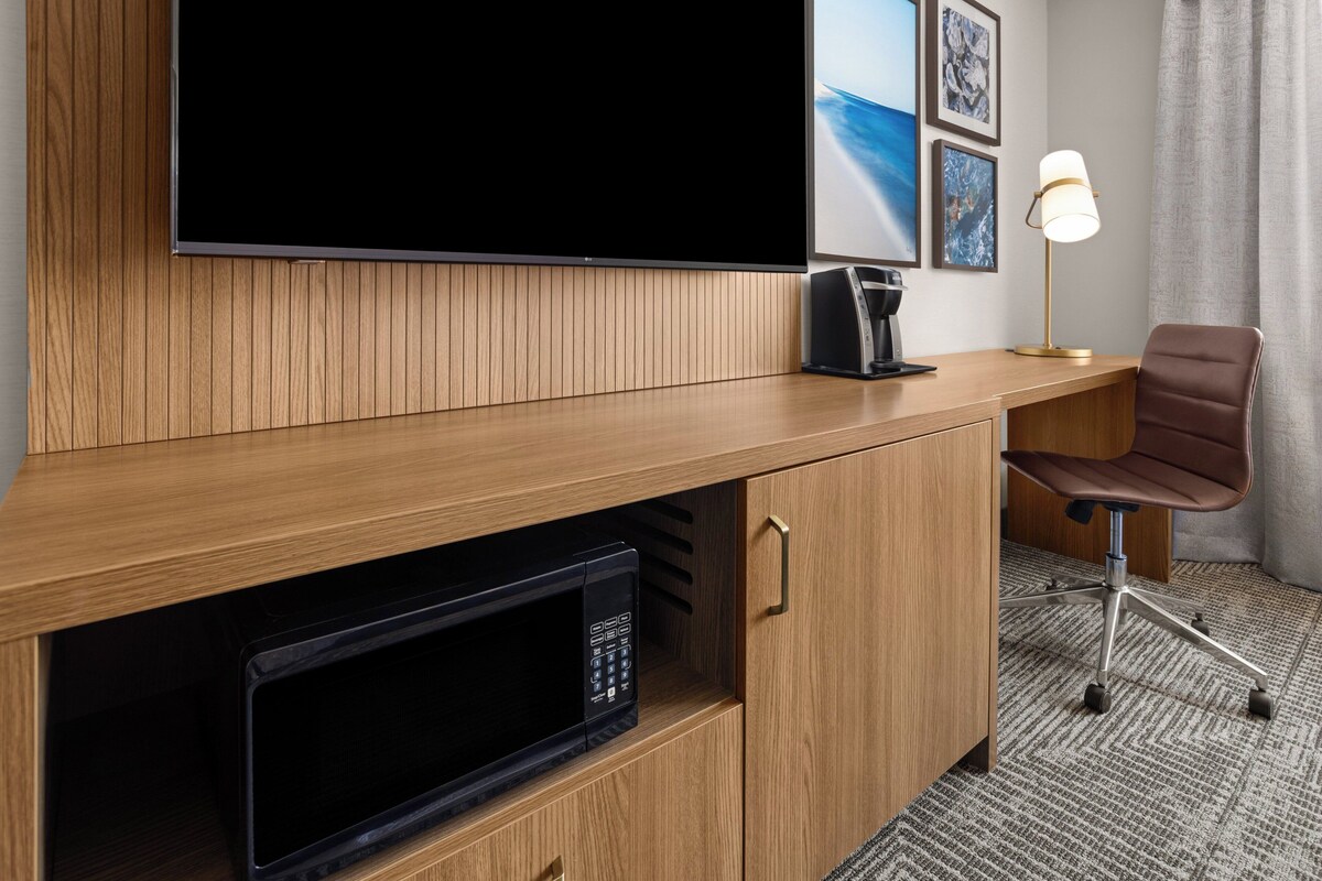 Une chambre d’hôtel équipée d’une télévision à écran plat, d’un four à micro-ondes, d’un bureau avec une chaise et d’une lampe.