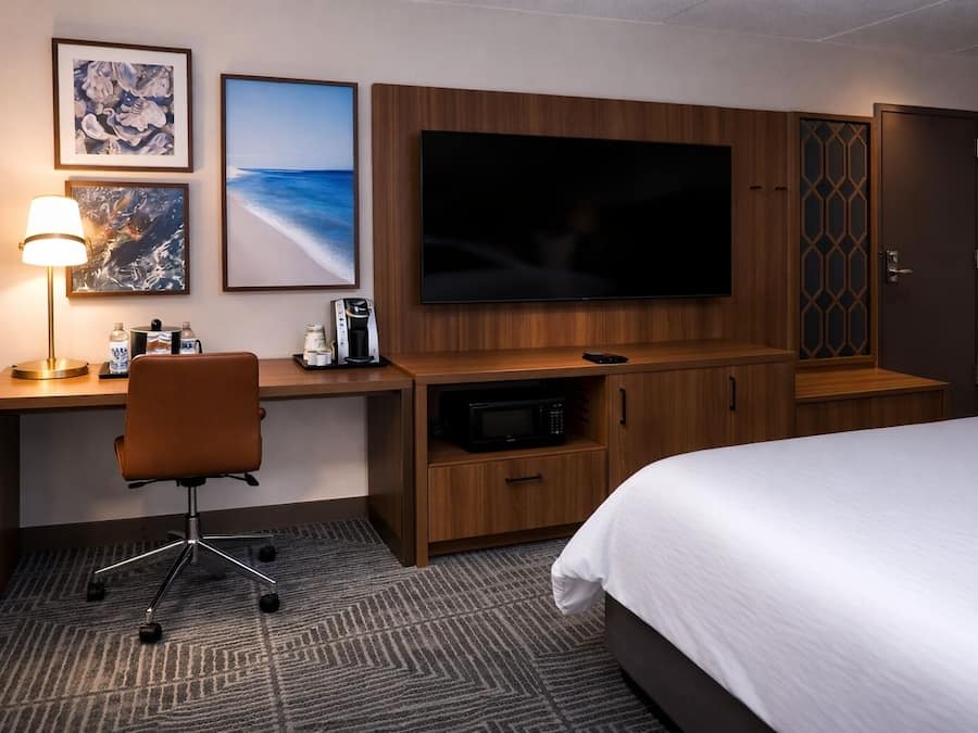 A hotel room with a bed, a desk with a chair, a TV, a coffee maker, and a microwave.