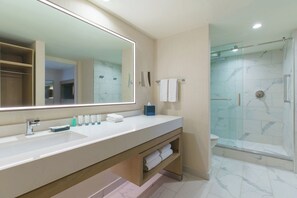 A modern bathroom with a large mirror, a shower, and a vanity with toiletries.