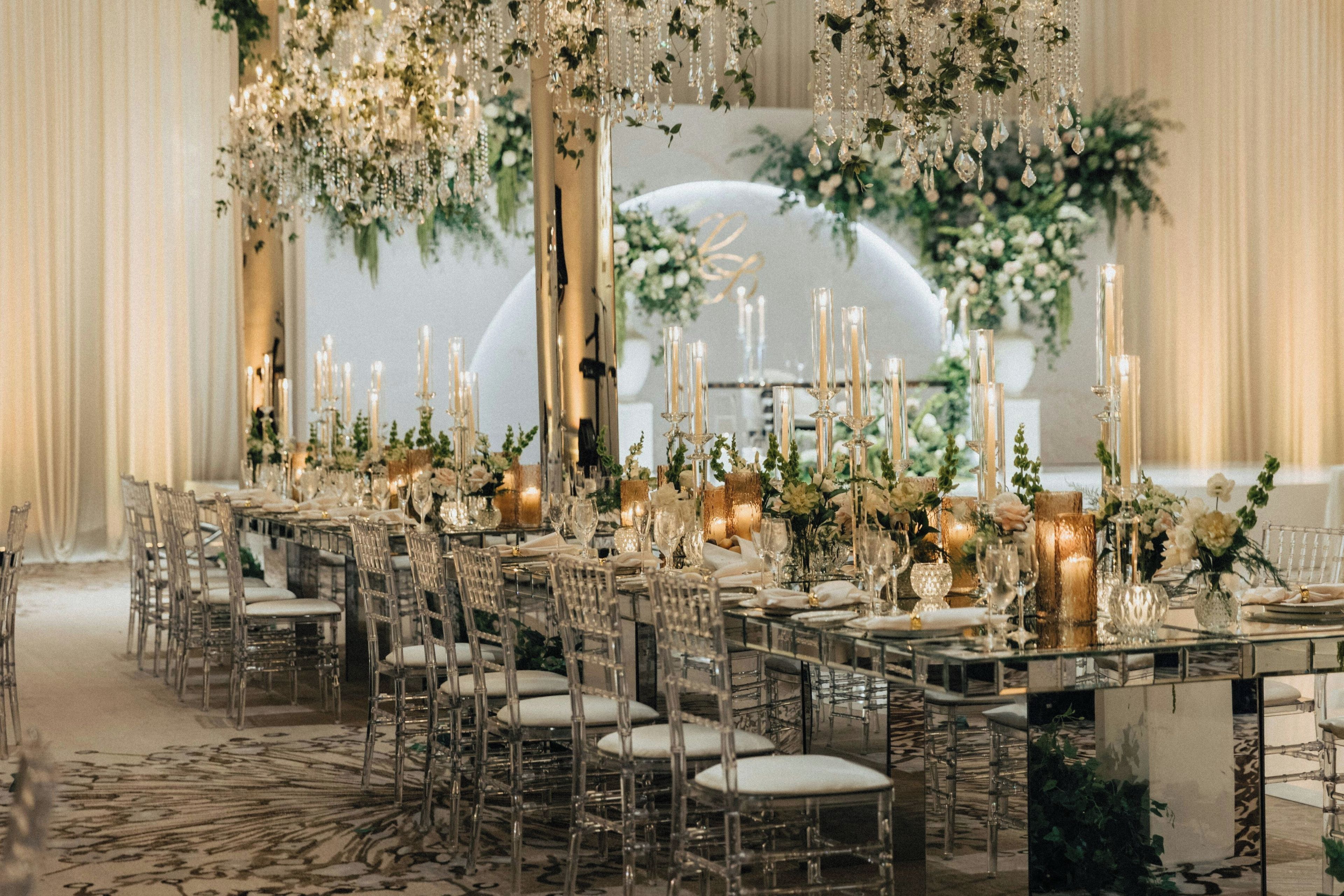 A banquet hall with a long table set for a formal event, surrounded by chairs and adorned with floral arrangements and candles.