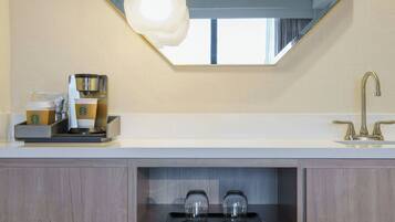 A modern bathroom with a large mirror, a coffee machine, and shelves with toiletries.