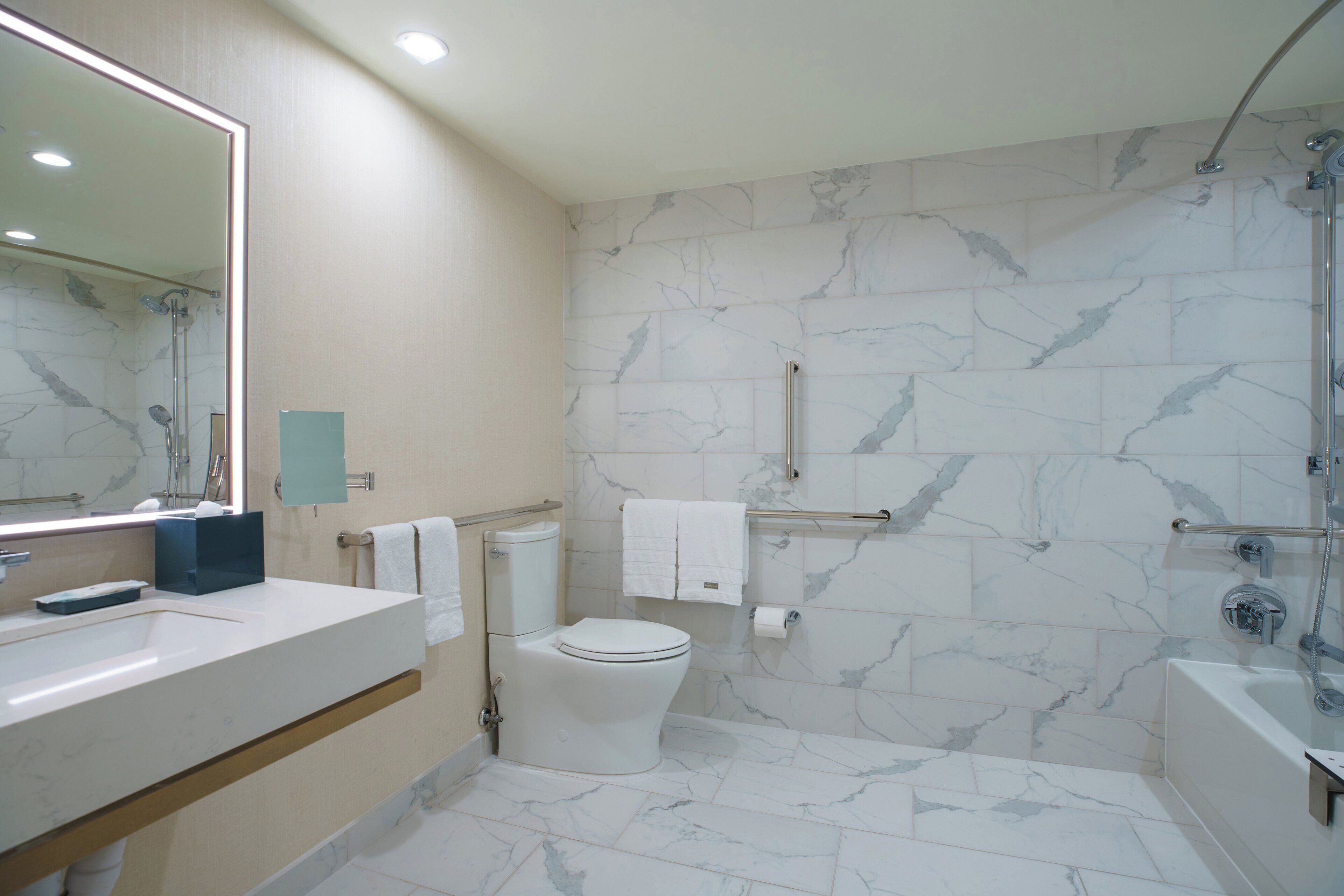 Un baño moderno con salpicadero de mármol, un espejo grande, una bañera y un inodoro.