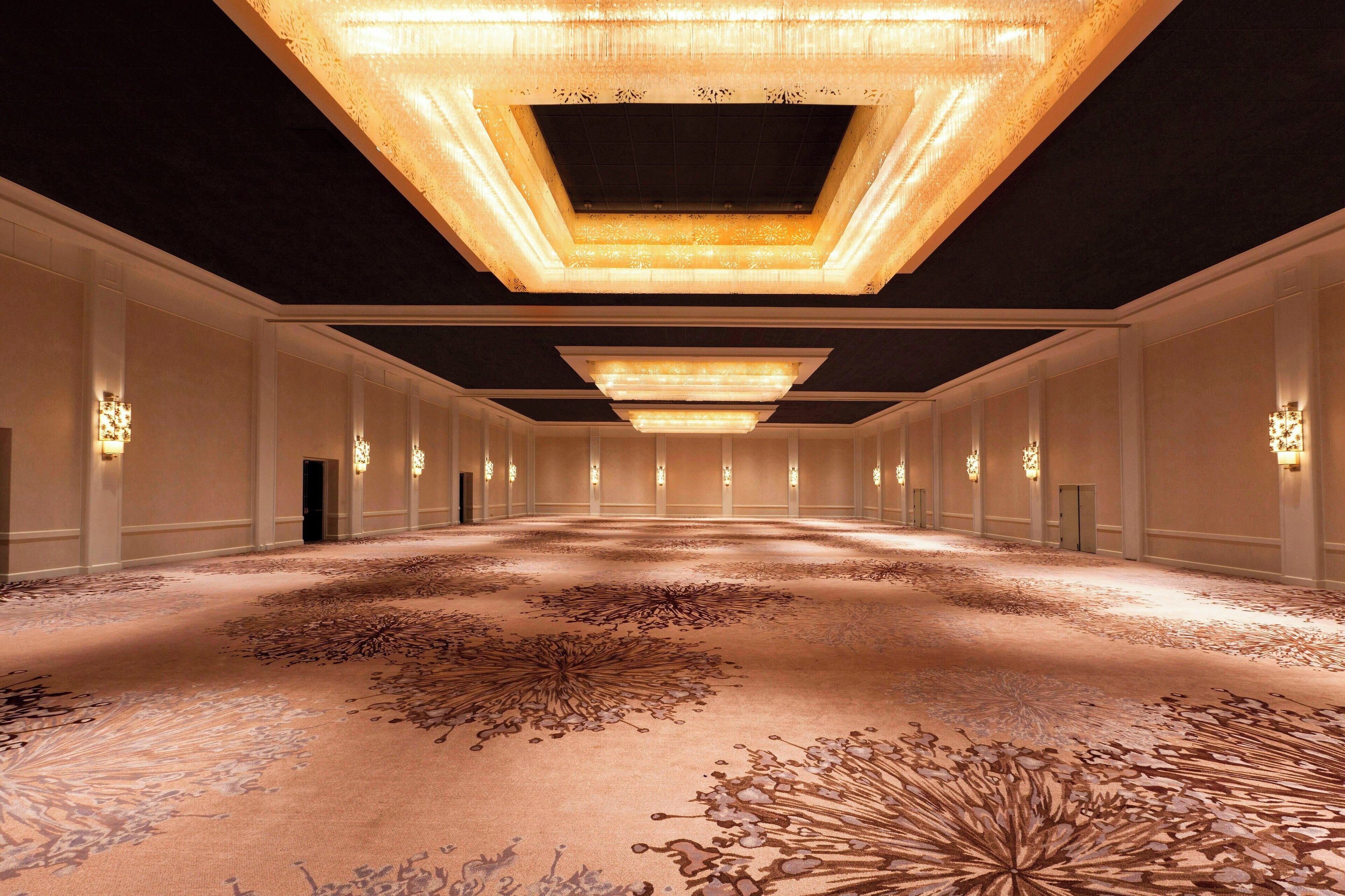 A spacious hotel lobby with a high ceiling, ornate chandeliers, and a detailed carpet design.