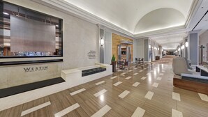 Eine moderne Hotelhalle mit einer Rezeption, einer Sitzecke und Blick in die Halle zum Geschäftsbereich.