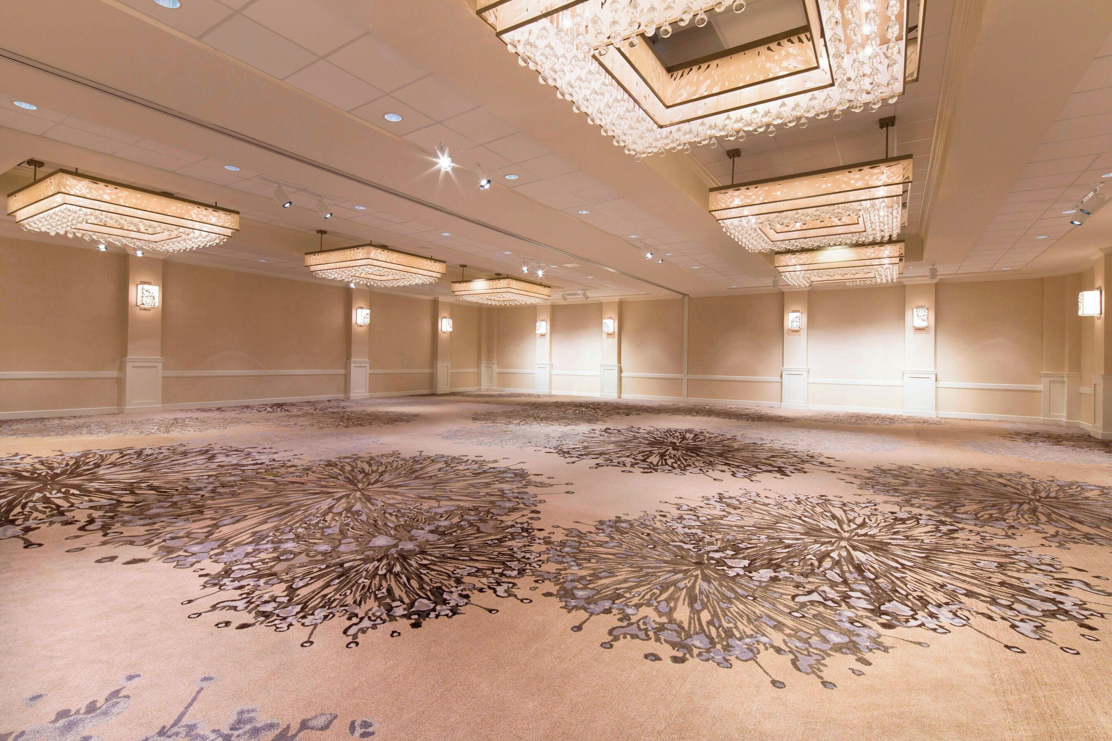 A spacious conference room with ornate chandeliers and a detailed carpet design.