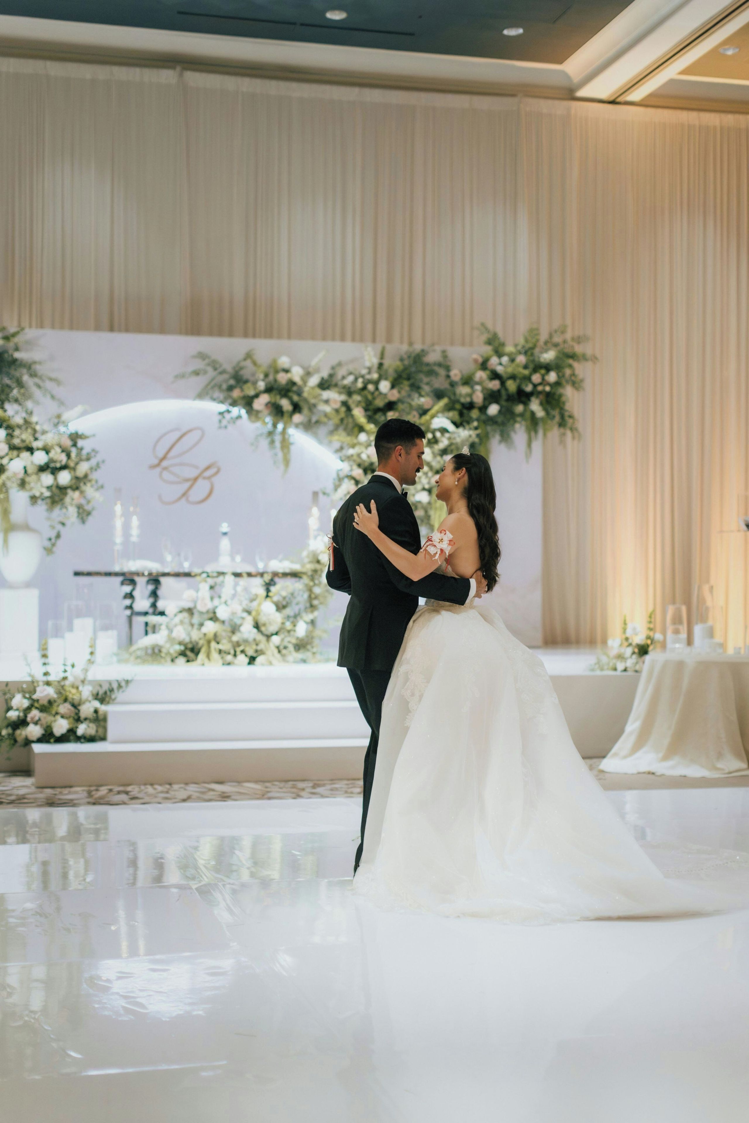 A couple embracing in a wedding ceremony with a floral backdrop and a stage with candles.