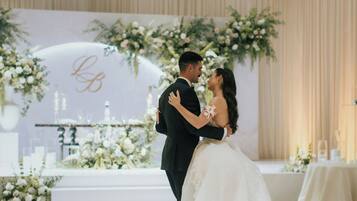 A couple embracing in a wedding ceremony with a floral backdrop and a stage with candles.