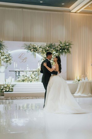 A couple embracing in a wedding ceremony with a floral backdrop and a stage with candles.