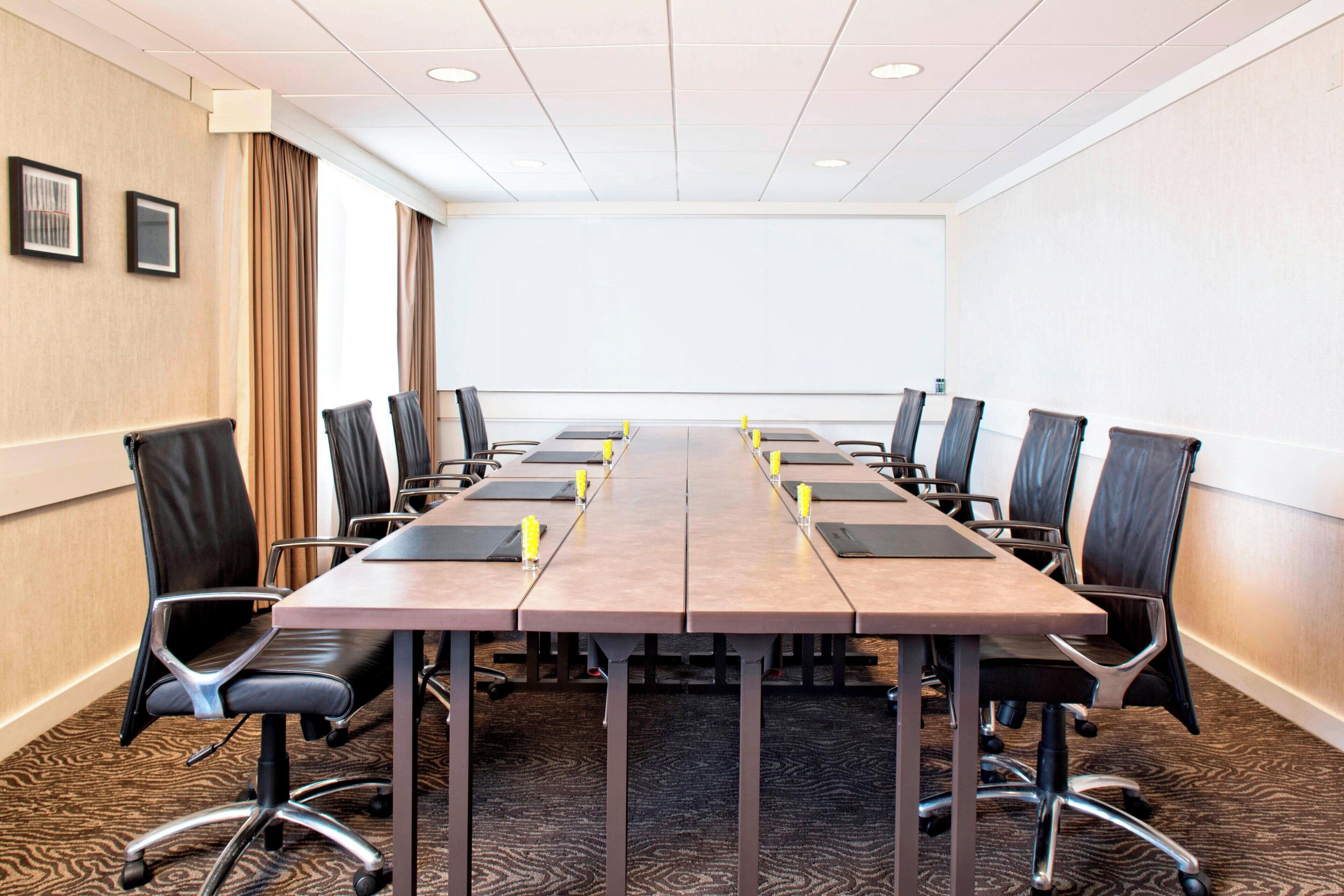 Une salle de conférence avec une longue table, des fauteuils en cuir noir et un sol recouvert de moquette.