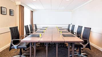 Une salle de conférence avec une longue table, des fauteuils en cuir noir et un sol recouvert de moquette.