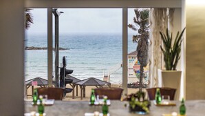 Un comedor con vista al océano, con una mesa dispuesta y botellas, y una planta en maceta.