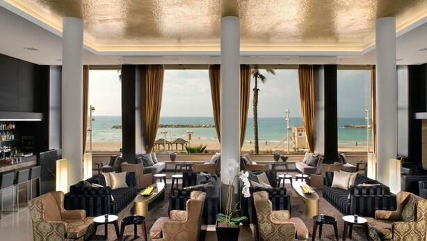 Amplia zona de estar con varias opciones de asientos, un bar y ventanas grandes con vistas a la playa y al océano.
