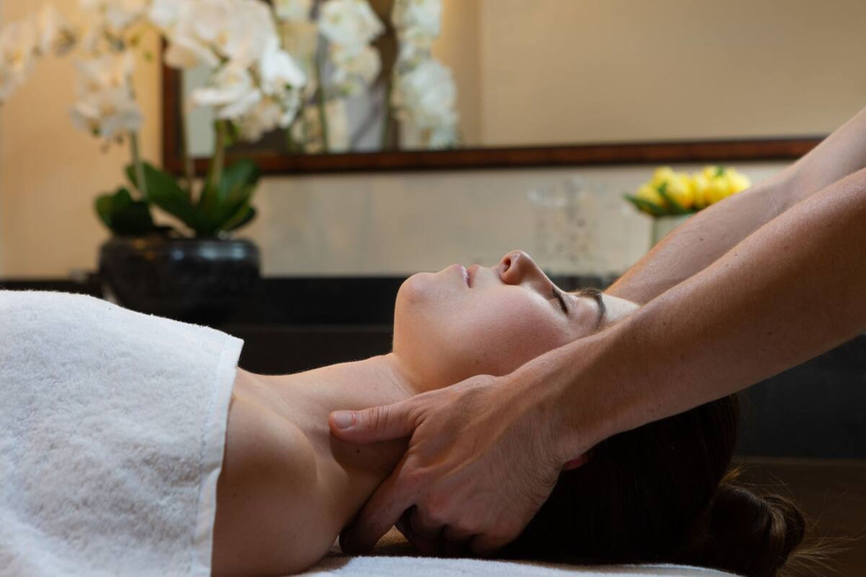 A person receiving a massage in a room with a large mirror and decorative flowers.
