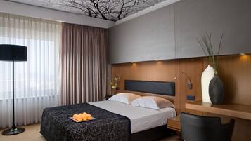 Ein modernes Hotelzimmer mit Bett, Schreibtisch, Stuhl, Lampe und einer Pflanze in einer Vase.