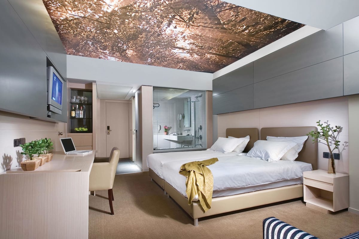 A modern bedroom with a bed, bedside tables, a desk, and a laptop.