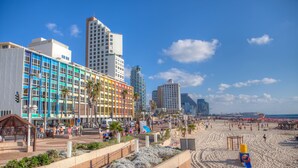 Un hotel frente a la playa con una fachada colorida, una playa en primer plano y edificios altos al fondo.