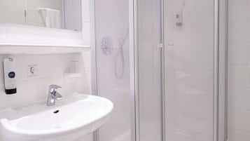 A modern bathroom with a white sink, a glass shower enclosure, and a white towel hanging on the wall.