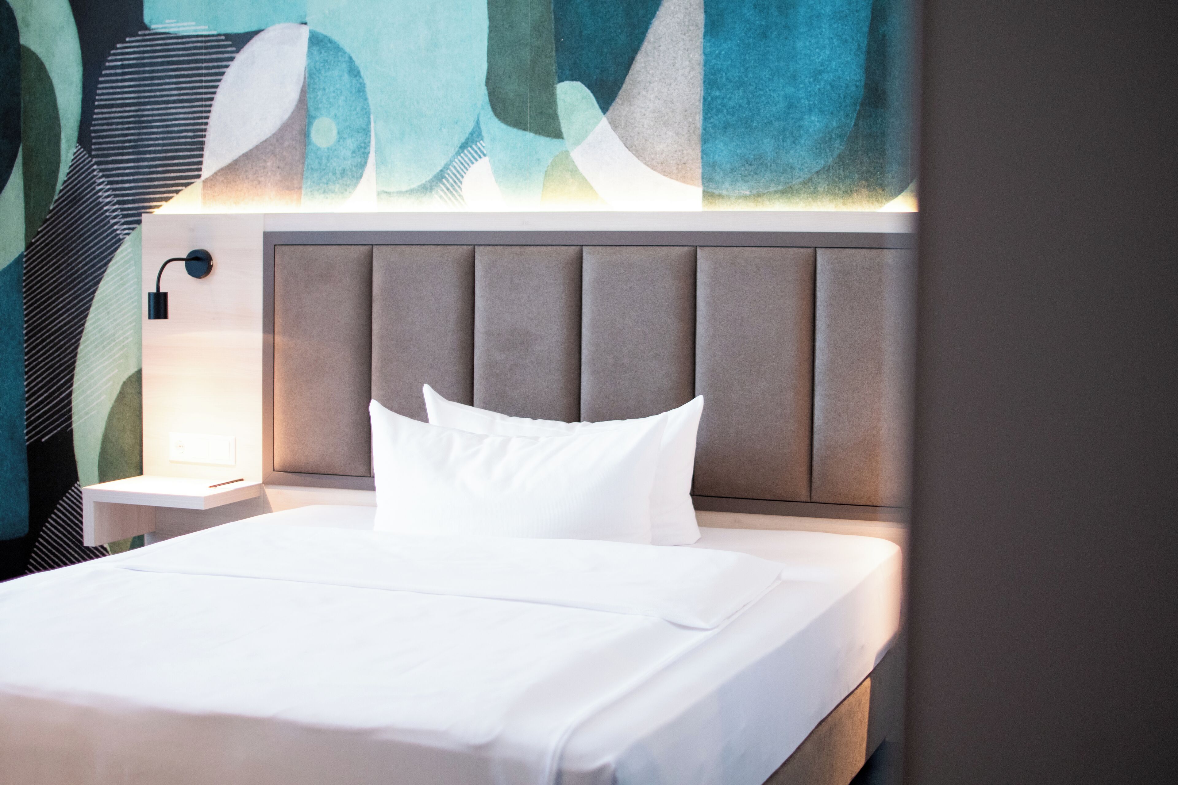 A neatly made bed with white linens and a headboard with vertical panels.