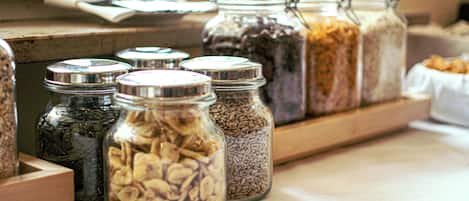 Glass jars with metal lids containing various grains and seeds on a wooden shelf.