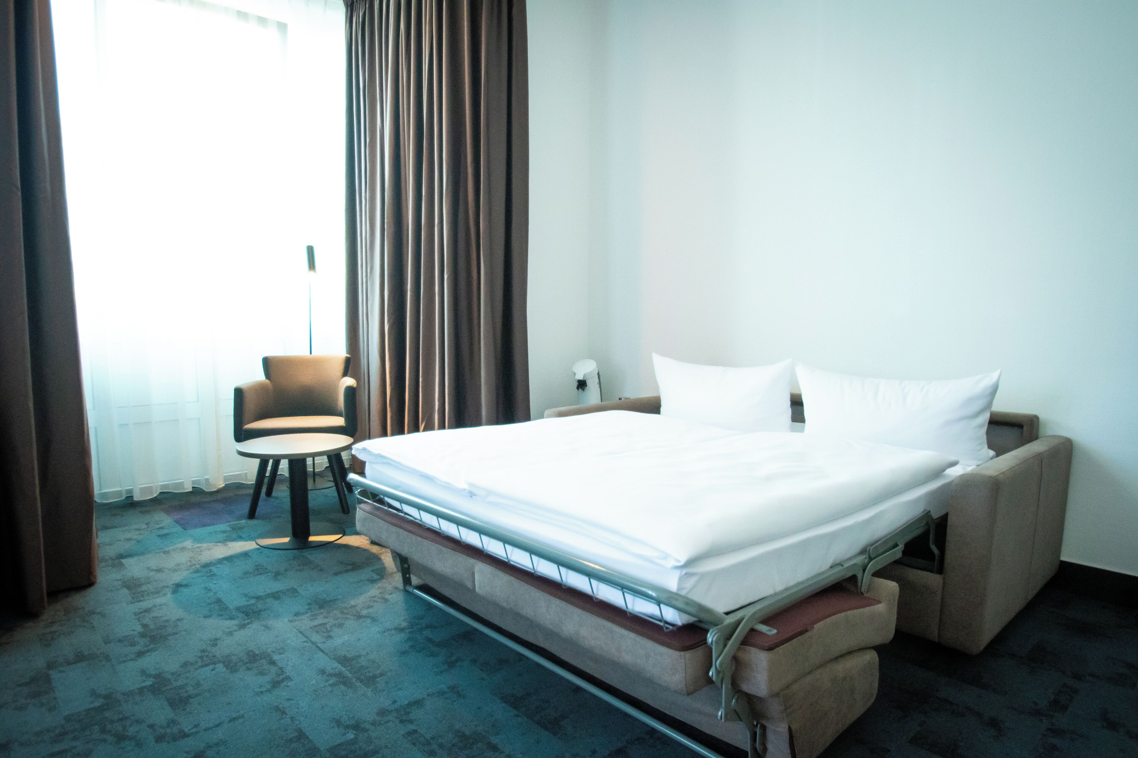 A hotel room with a bed, a chair, and a window with curtains.