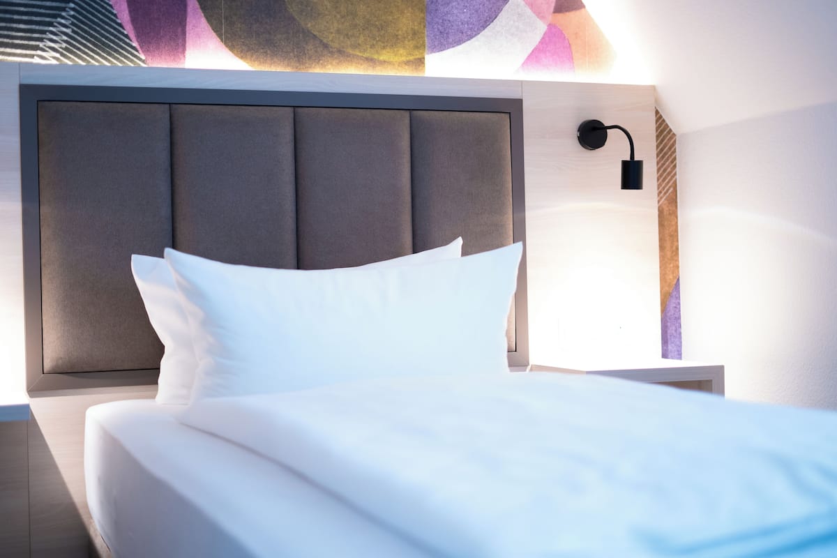 A neatly made bed with white linens in a modern hotel room.