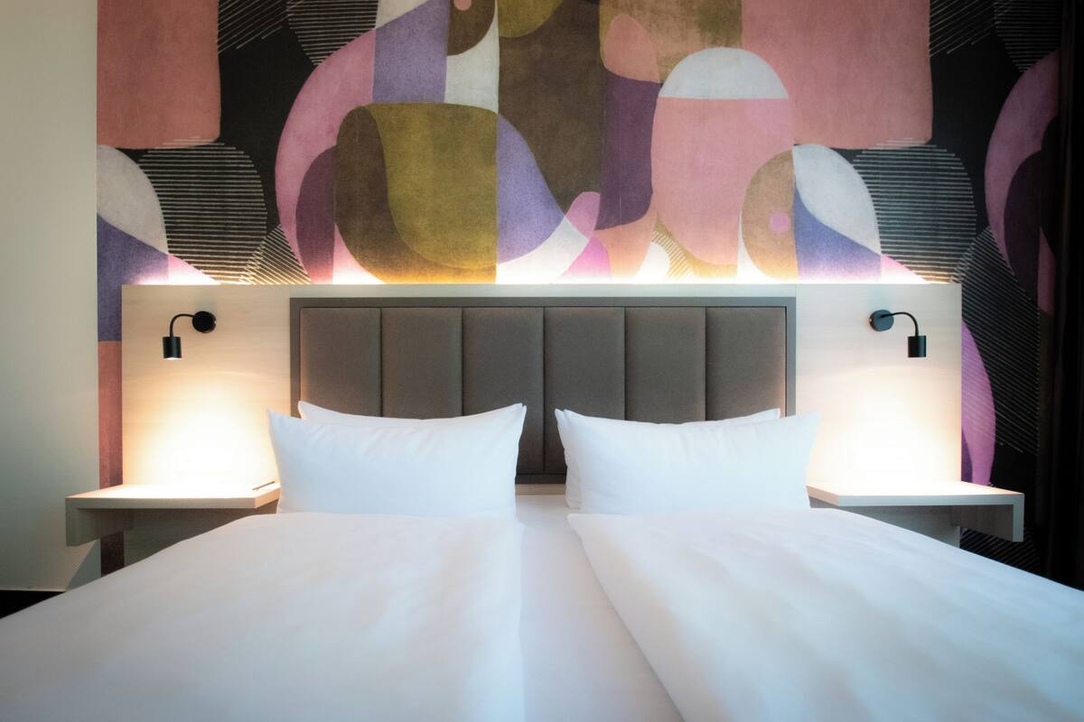 A hotel room with a large bed, two bedside lamps, and a modern abstract wall design.