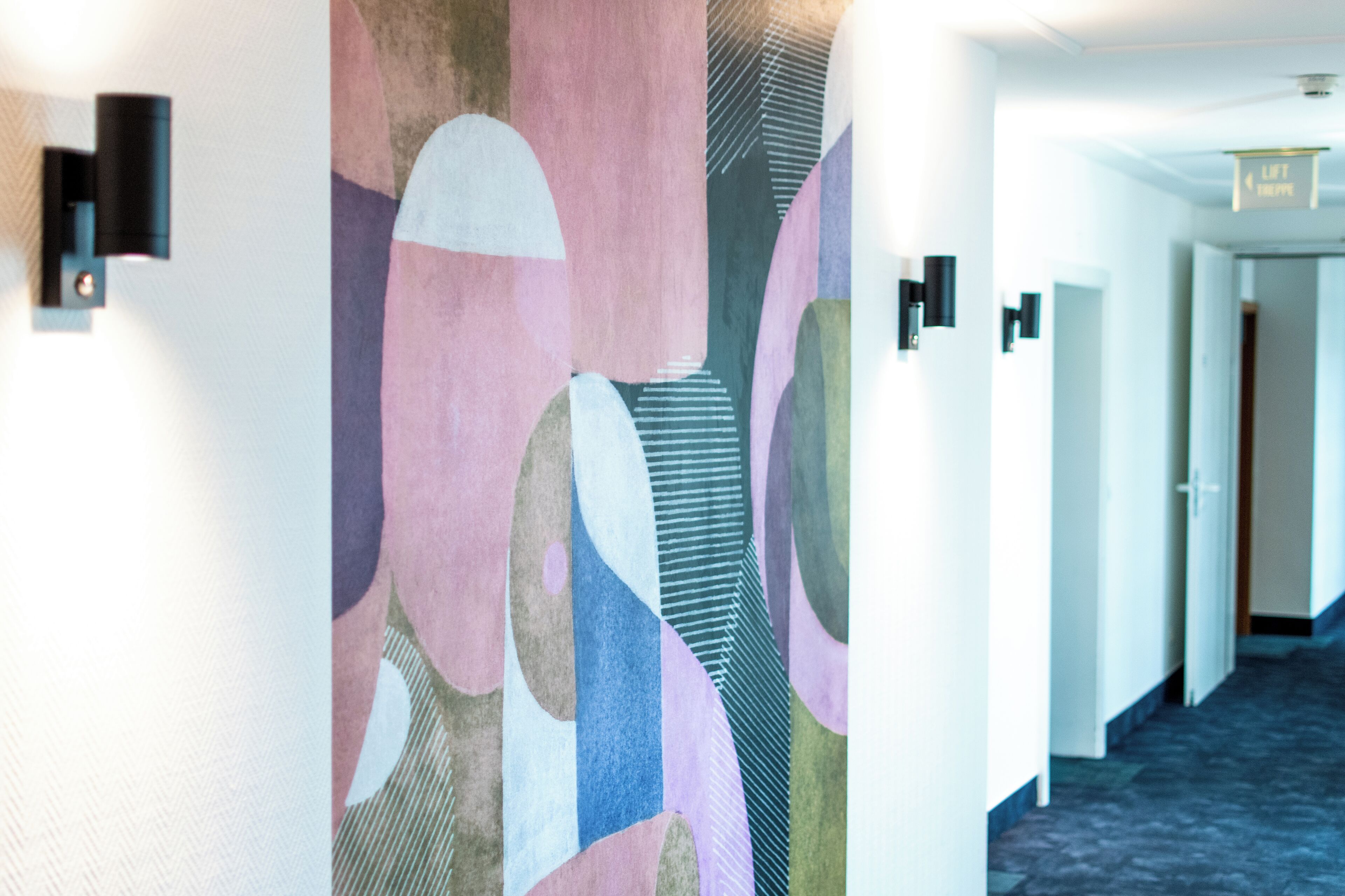 A hallway with abstract wall art, a patterned carpet, and a door with a sign that reads "Lift Exit."