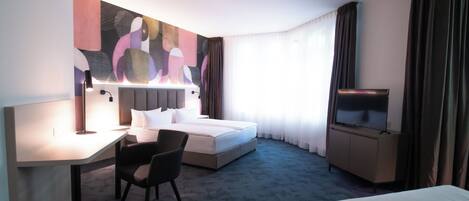 A hotel room with a bed, a desk, a chair, a TV, and a large abstract painting on the wall.