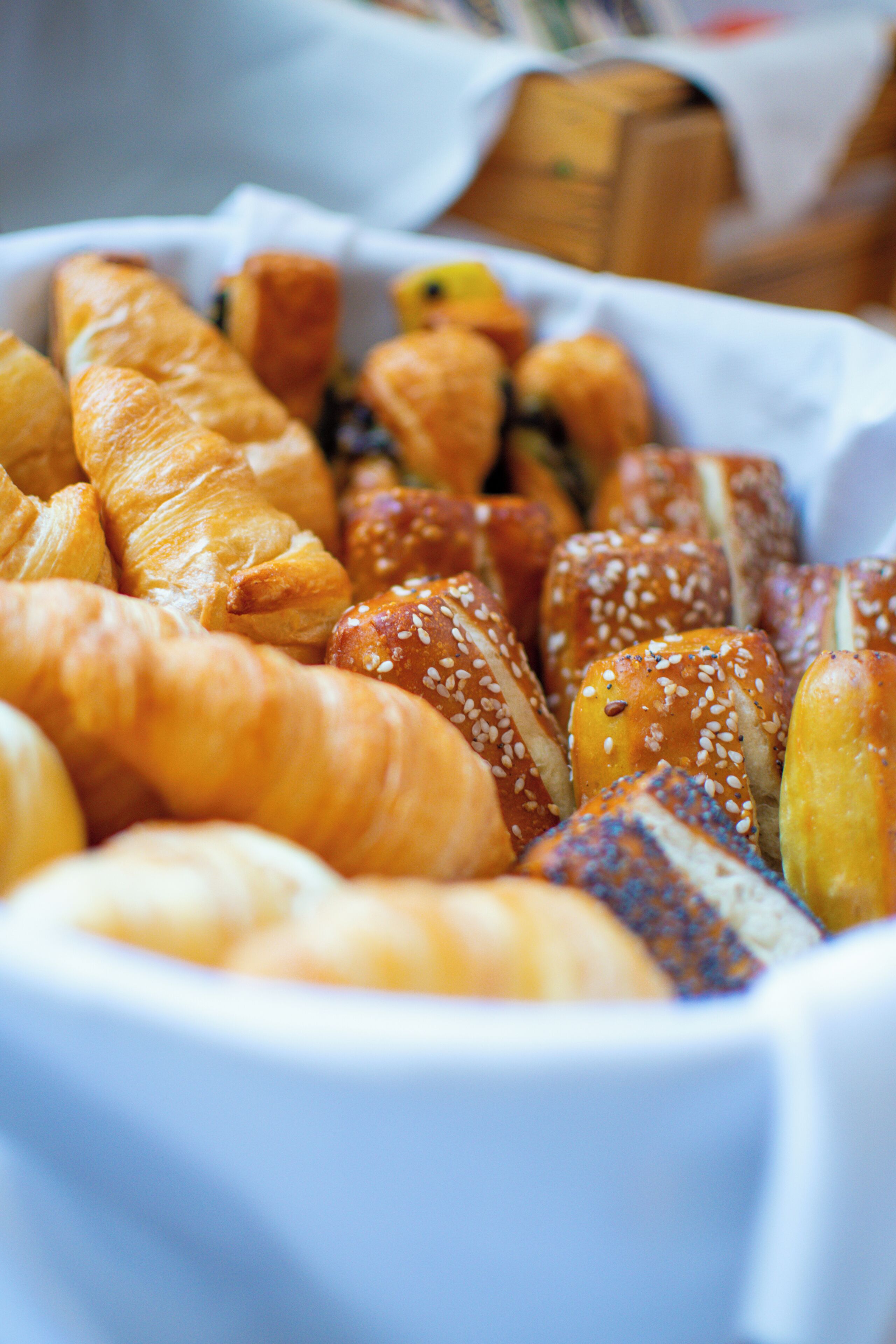 A variety of baked goods, including croissants and bread rolls, arranged in a white basket.
