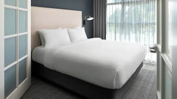 A neatly made bed with white linens, a headboard, and a bedside lamp.