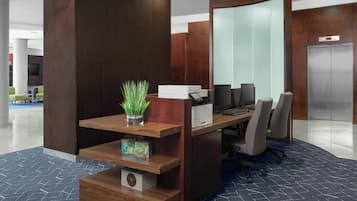 A modern reception desk with a plant, a printer, and a computer. There are several chairs and a large mirror.