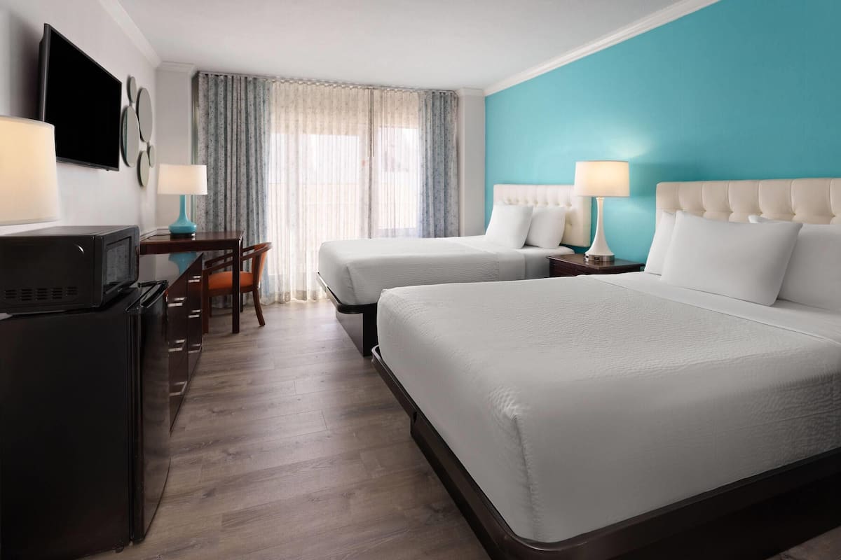 Une chambre d’hôtel avec deux lits, un bureau avec une télévision et un coin repas avec des chaises.
