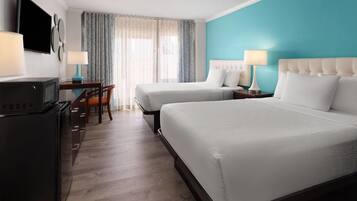 A hotel room with two beds, a desk with a TV, and a dining area with chairs.
